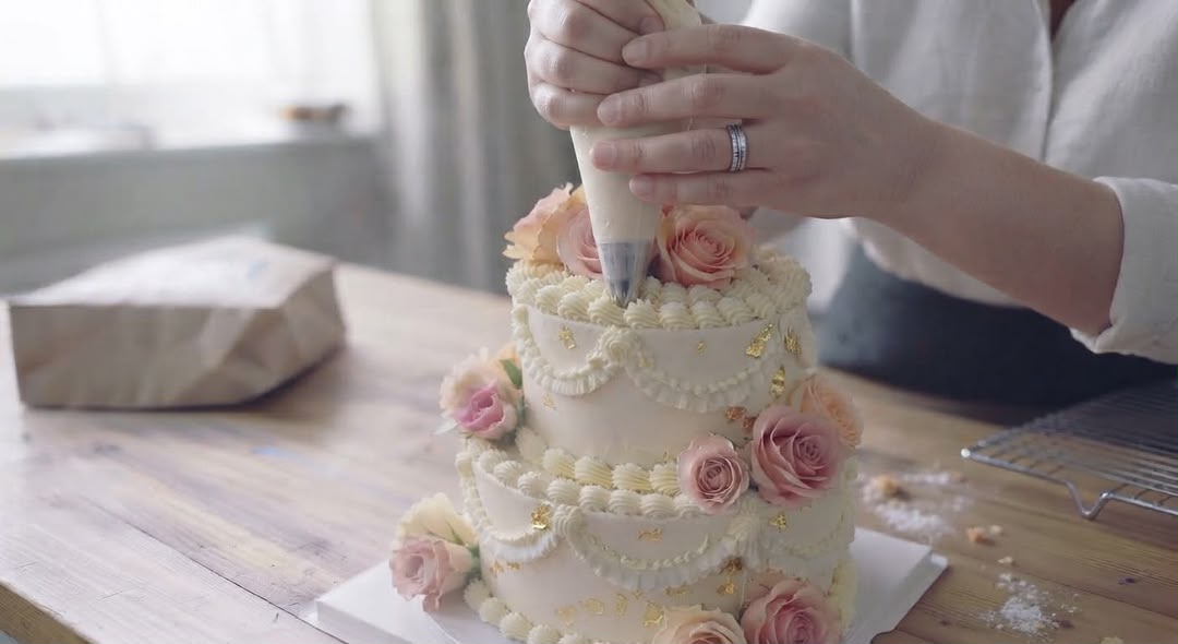 Piping buttercream and adding florals to a celebration cake